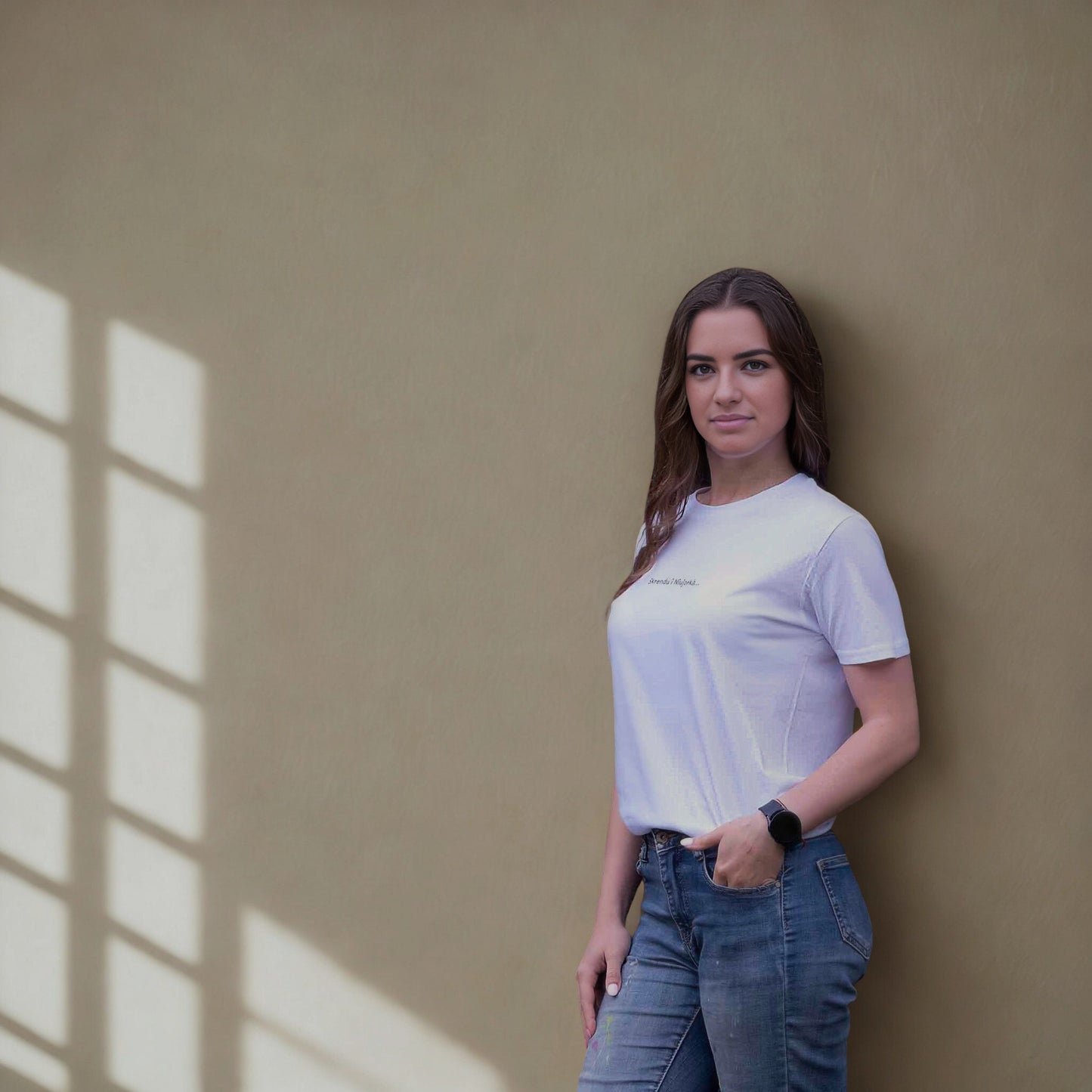 Moteris dėvinti baltus marškinėlius „Skrendu i Niujorkà“ šalia lango šviesoje