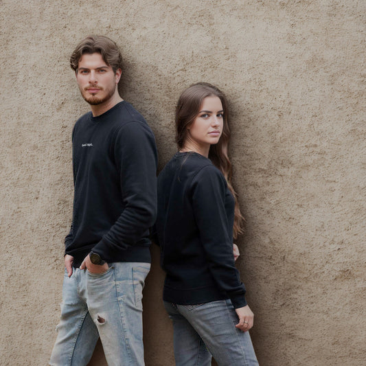 Unisex džemperis be kapišono „Skrendu i Niujorkà“, dėvi vyras ir moteris, stovintys prie sienos