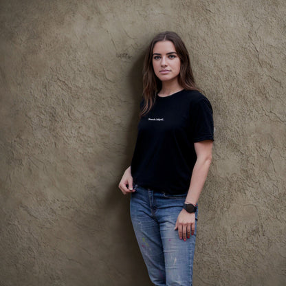 Unisex juodi marškinėliai „Skrendu i Niujorkà“ ant moters modelio prie sienos